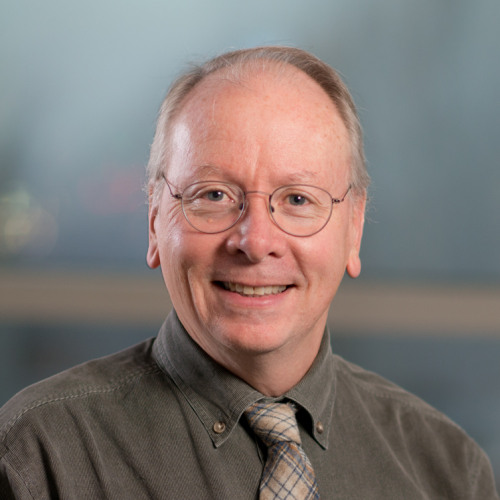 Professor Karl Kelsey smiles at camera while posing in front of windows. 