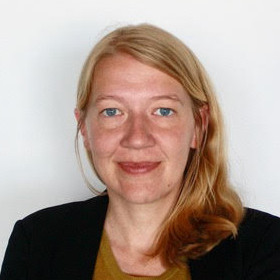 Professor Rachel Baker smiles at camera while posing in front of a white background.